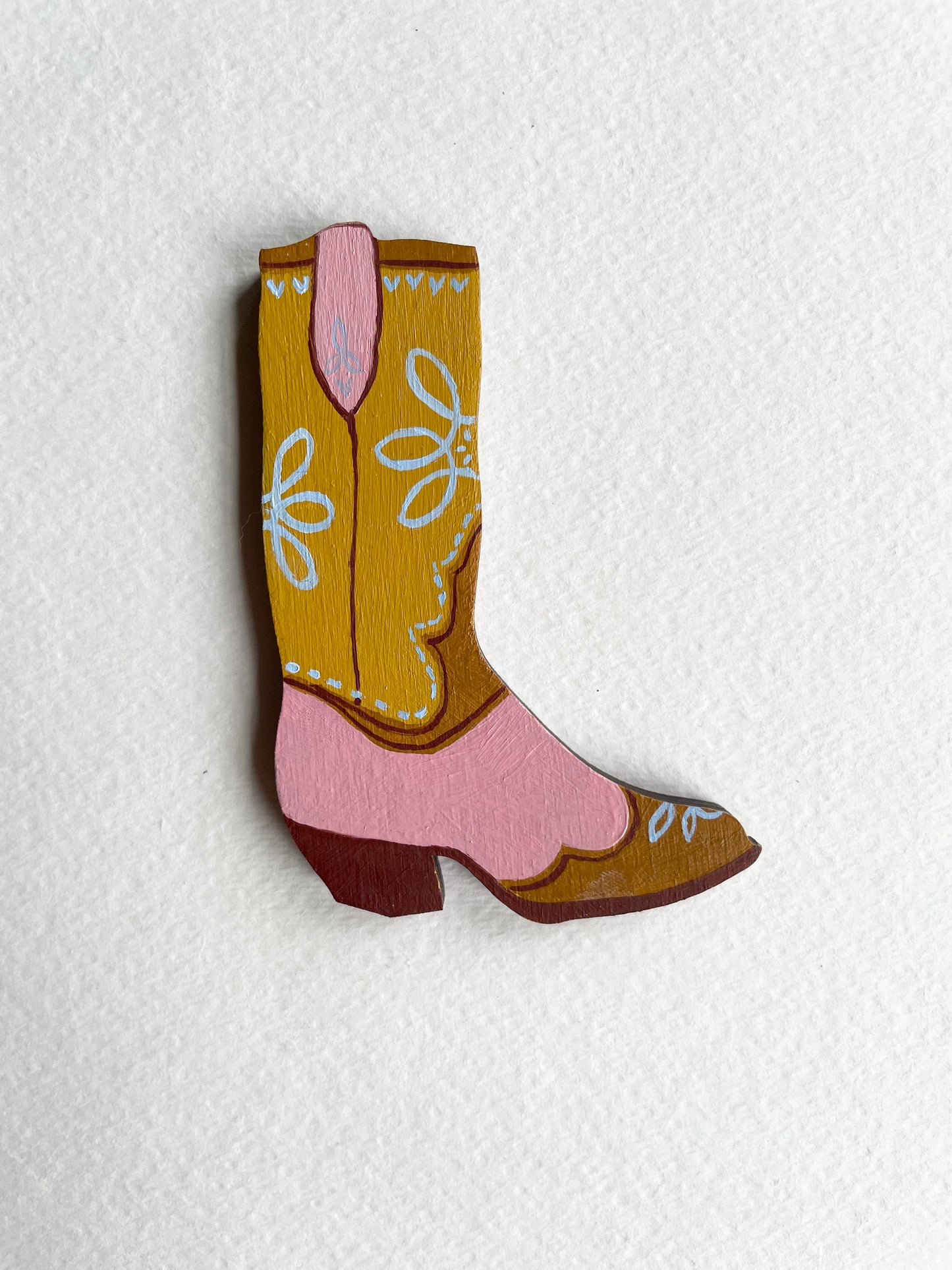 Wooden cowboy boot with pink interior on a textured white background