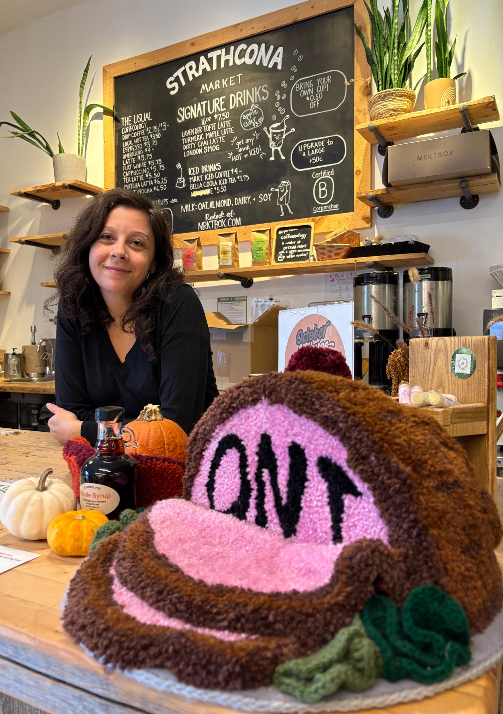 Woman standing behind a large knitted cake with 'OPI' branding in a market setting.