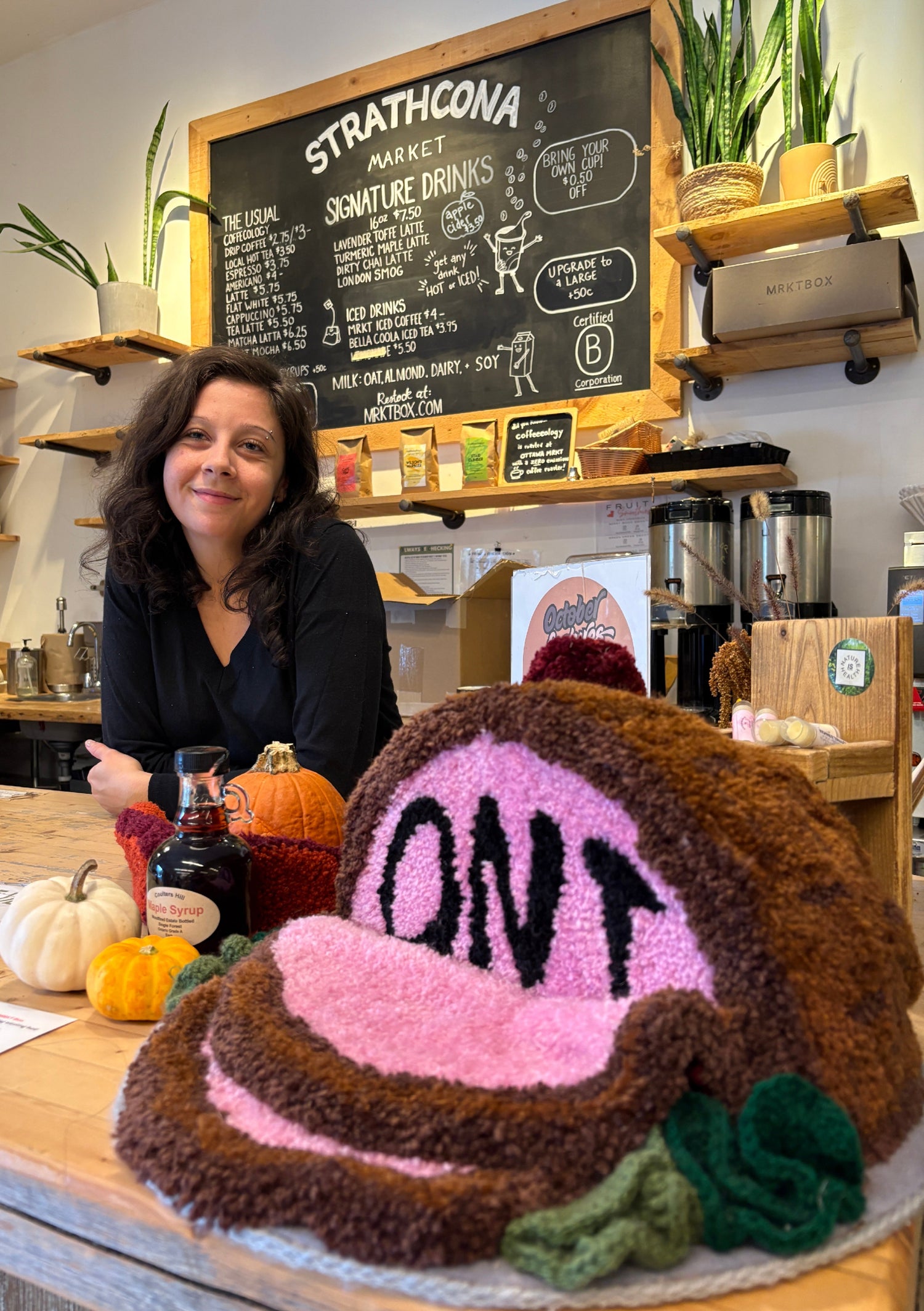 Woman standing behind a large knitted cake with 'OPI' branding in a market setting.